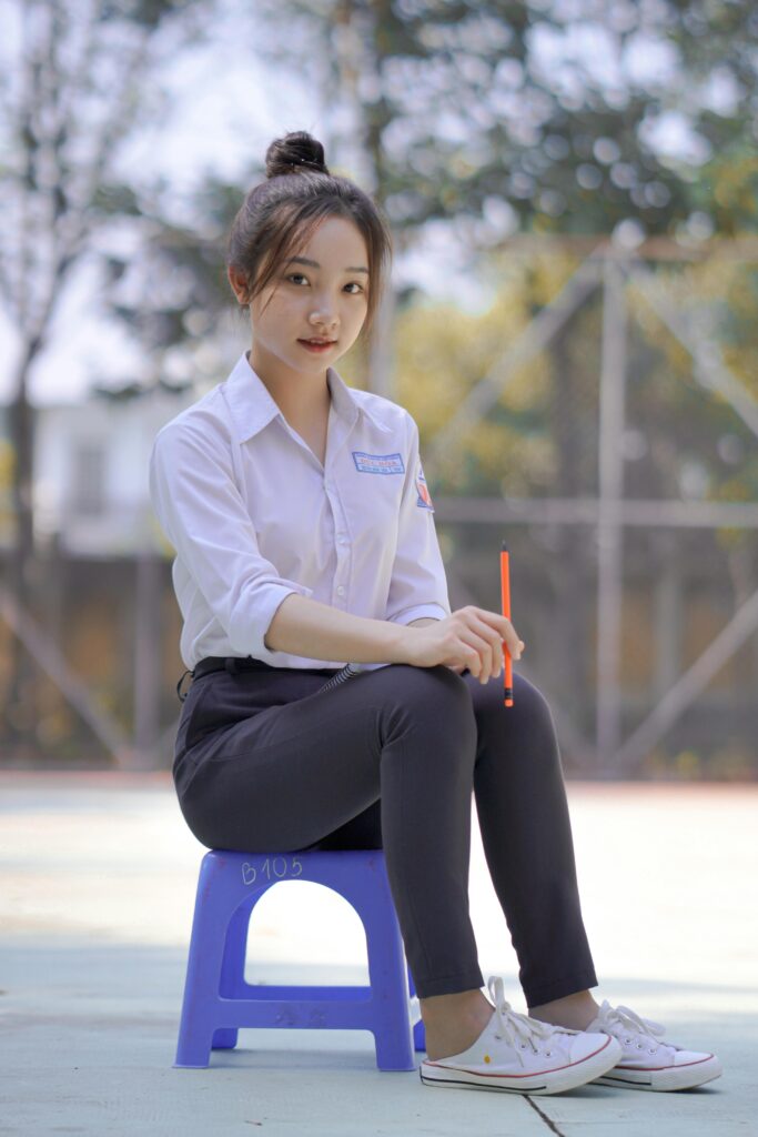 pexels-photo-21006302-21006302 Confident young woman wearing a school uniform seated outdoors on a bright day.
