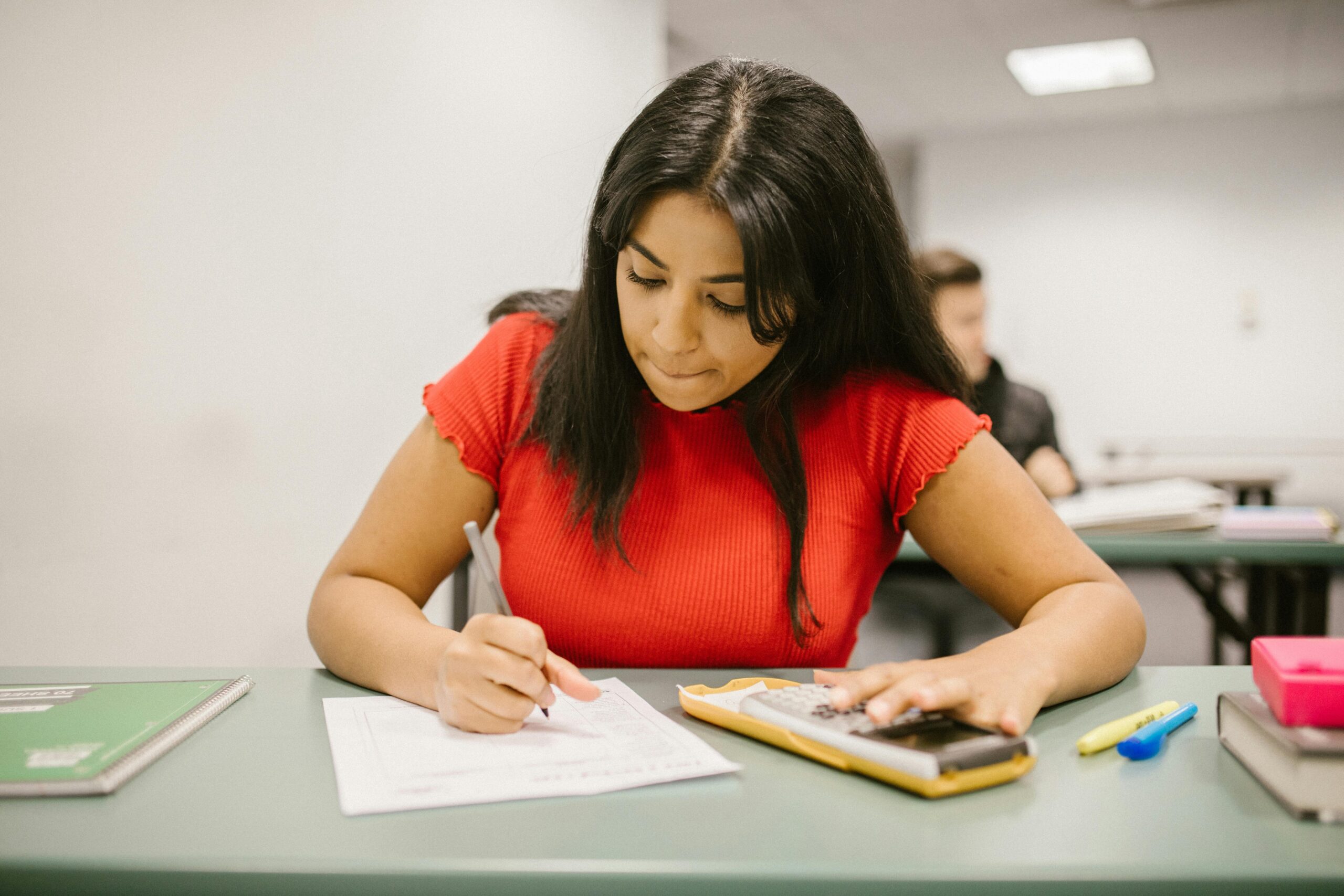 Focused college student using a calculator during an exam. Indoor educational setting.