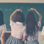 Group of teenage girls in school uniforms enjoying time together in a classroom, posing with playful gestures.
